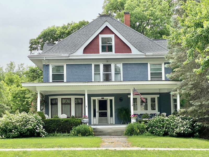 Built around the turn of the 20th Century, this Queen Anne-style house features a shingle and clapboard exterior with a hipped roof featuring a flared lower portion and broad overhanging eaves, stucco-clad gables on the front and side facades,