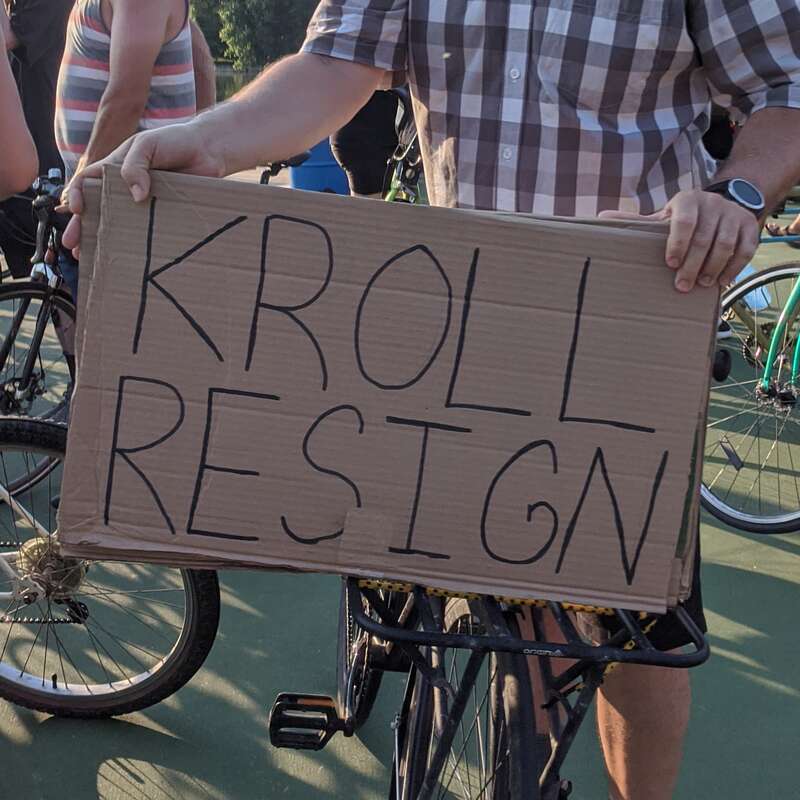 A protestor at a July 4th roll-through rally in Minneapolis holds a sign reading 'Kroll Resign.' 
Photo taken at Bde Maka Ska in Minneapolis, Minnesota.