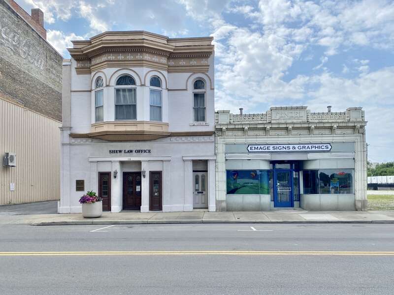 On the left, built in 1896, this Queen Anne-style building is known as the Shew Building, after its present tenant, the Shew Law Office.  The building features a painted brick exterior, an architrave with fleur-de-lis, a cornice with dentils,