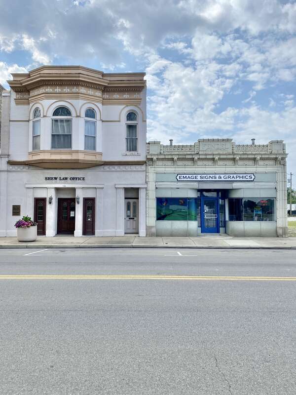 On the left, built in 1896, this Queen Anne-style building is known as the Shew Building, after its present tenant, the Shew Law Office.  The building features a painted brick exterior, an architrave with fleur-de-lis, a cornice with dentils,