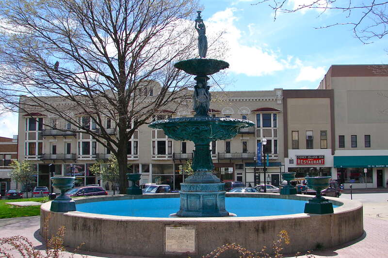 Vasbinder Fountain in Mansfield Ohio.  Behind the fountain (to the left behind the tree) is the May Realty Building on the NRHP since October 16, 1986, at 22-32 S. Park St., Mansfield, Ohio.
The buildings to the right are the Coney Island Inn (#20 S.