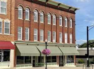 Built around the turn of the 20th Century, this Romanesque Revival and Italianate-style building features a red brick facade, bracketed cornice, low slope rear shed roof with a parapet, brick pilasters between the window bays, arched window bays not