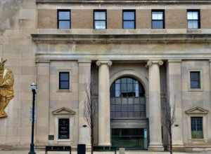 As seen in downtown Pontiac, Michigan, December 2020: a pair of proud Ionic columns flank a spacious arched portal at the grand entrance to the Neoclassical-styled 30 North building, located at the northeast corner of Saginaw and Lawrence Streets. At