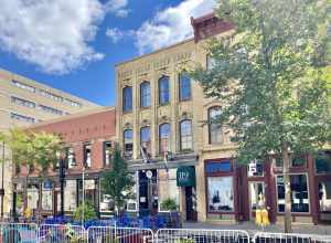 On the left, built in 1868, this Italianate-style building is known as Thompson’s Block, and features a buff brick exterior with limestone pilasters flanking the storefronts on the first floor, which feature cast iron columns, arched four-over-four