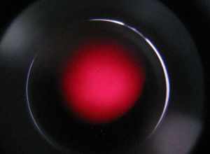 Viewed through H-alpha (Hα) filter telescope.  H-alpha is a specific red visible spectral line created by hydrogen with a wavelength of 656.28 nm, which occurs when a hydrogen electron falls from its third to second lowest energy